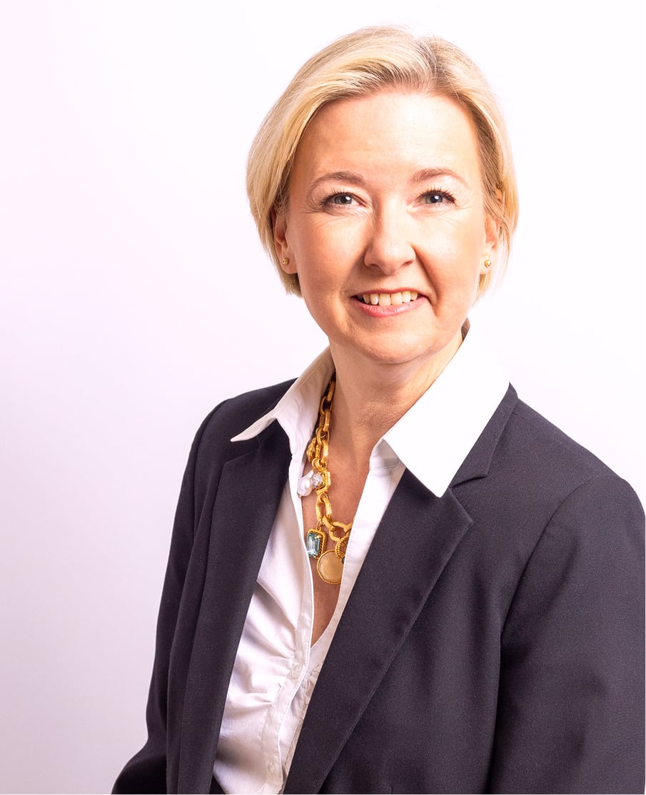 Angela Schuh-Haunold im Business-Porträt mit dunklem Blazer, weißem Hemd und goldenem Schmuck
