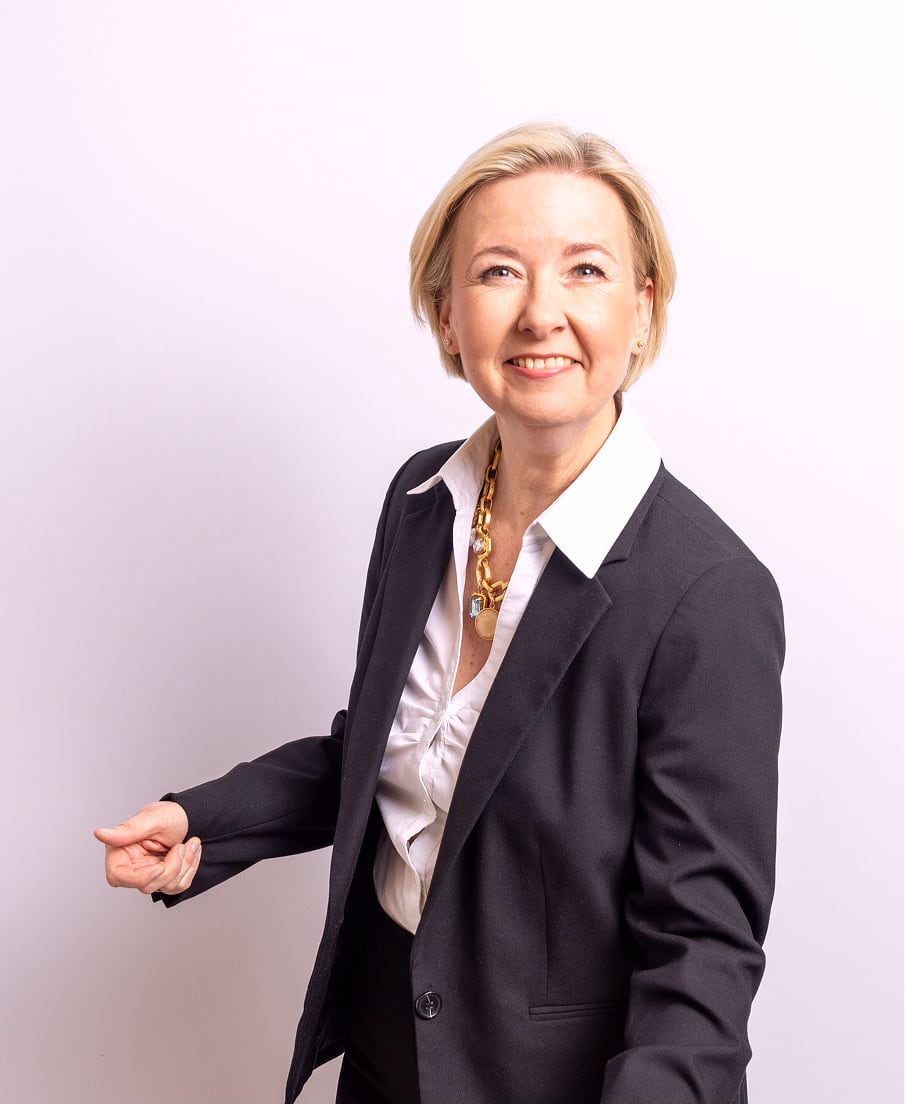 Angela Schuh-Haunold im dunklen Blazer, lächelnd mit einladender Handbewegung